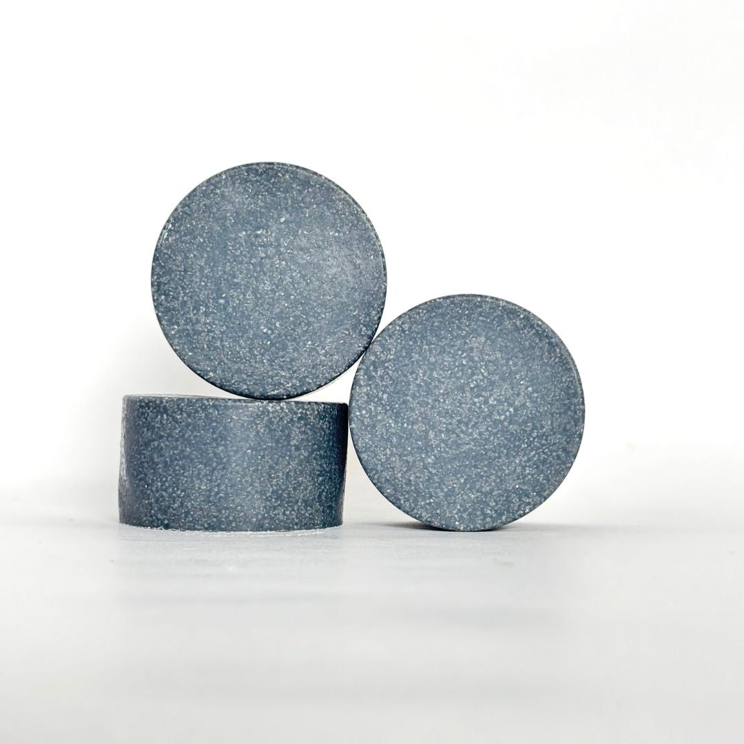 Front view of round Charcoal Detox Himalayan Salt Scrub Bar on another bar lying down with another bar beside against a white background