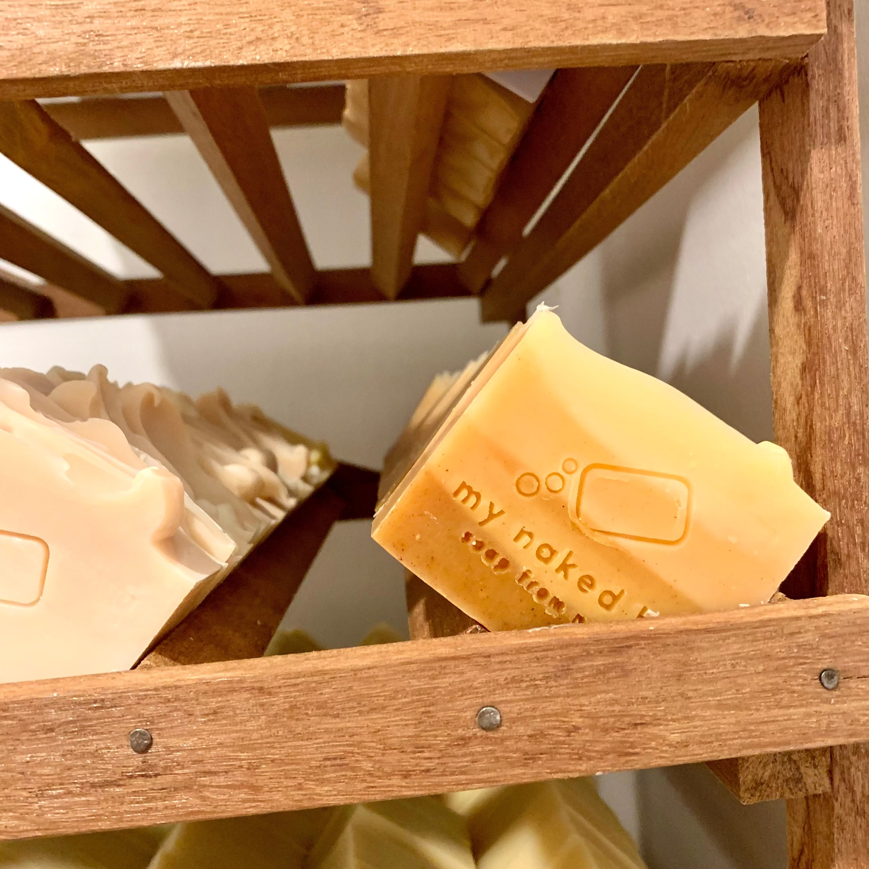 Rows of My Naked Bar soaps resting slanted on a wooden curing rack