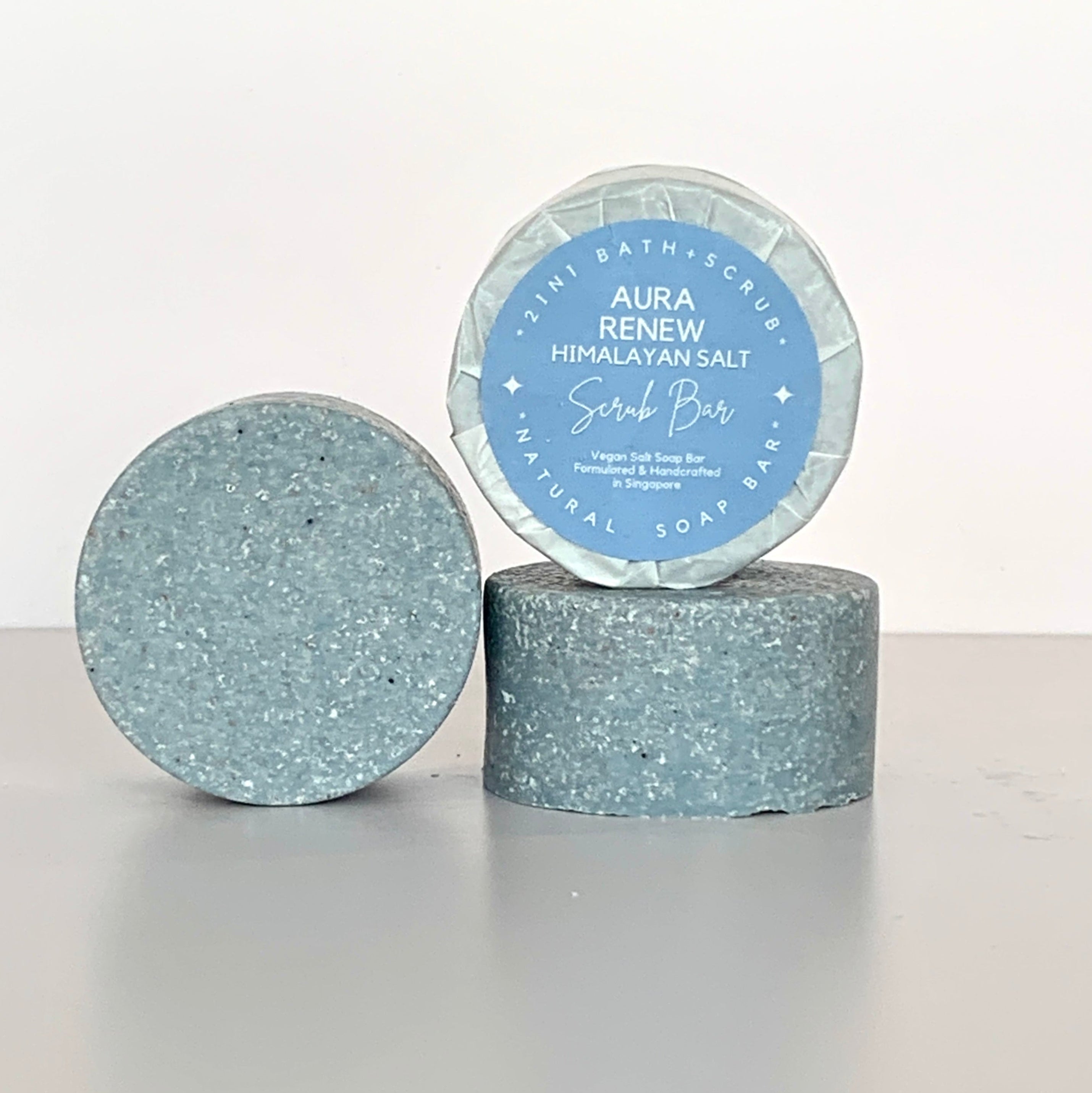 Front view of round Aura Renew Himalayan Salt Scrub Bar on another bar lying down with another bar beside against a white background